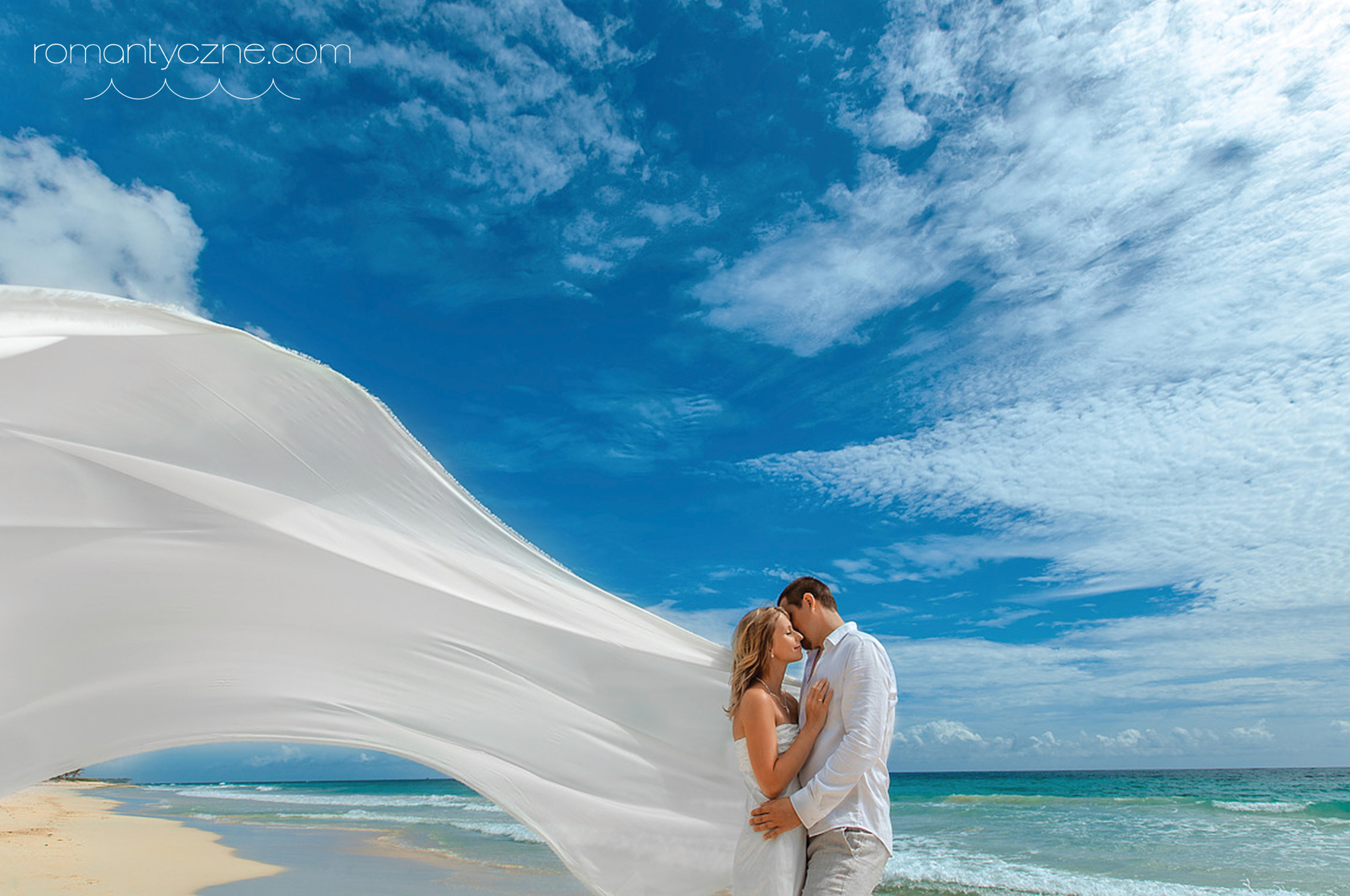 młoda para całująca się na rajskiej plaży - wiatr rozwiewa szal panny młodej