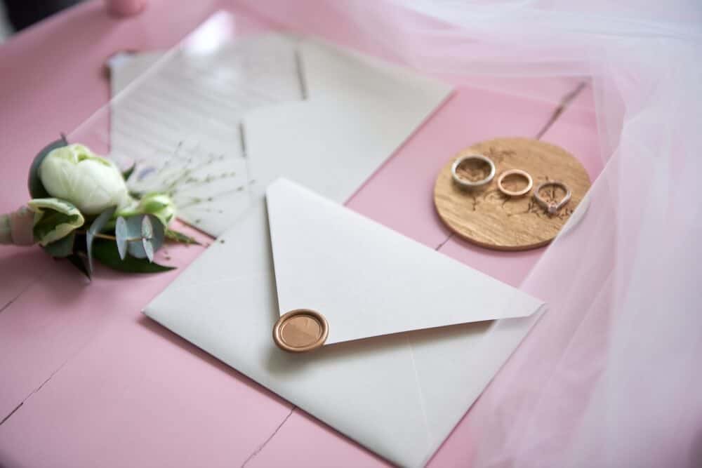 zaproszenie ślubne w białej kopercie na różowym tle