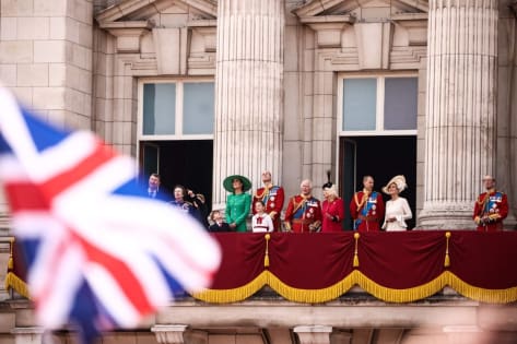 Brytyjska rodzina królewska na balkonie Pałacu Buckingham podczas oficjalnej uroczystości, flaga Wielkiej Brytanii z przodu.