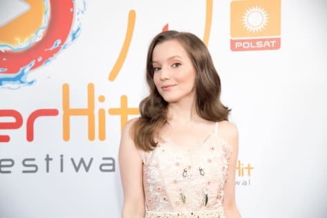 Alt: Kobieta w eleganckiej sukni na tle ścianki z logo SuperHit Festiwal i Polsat.