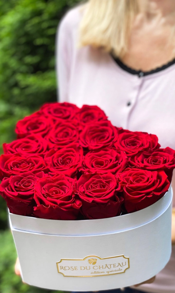 Pudełko z czerwonymi różami Rose du Château trzymane przez kobietę na tle zieleni.