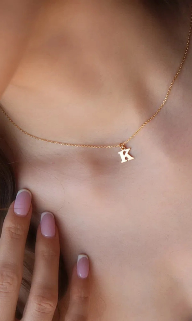 Naszyjnik złoty z zawieszką w kształcie litery K na szyi, delikatny manicure francuski.