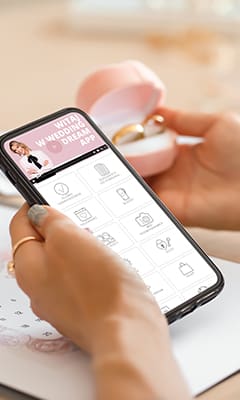 Osoba trzymająca telefon z aplikacją ślubną Wedding Dream, obok pudełko z obrączką.